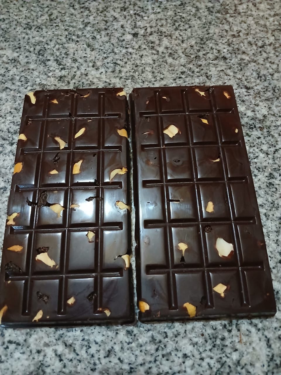 Two finished dark chocolate bars studded with pieces of Peruvian superfoods, resting on a stone counter