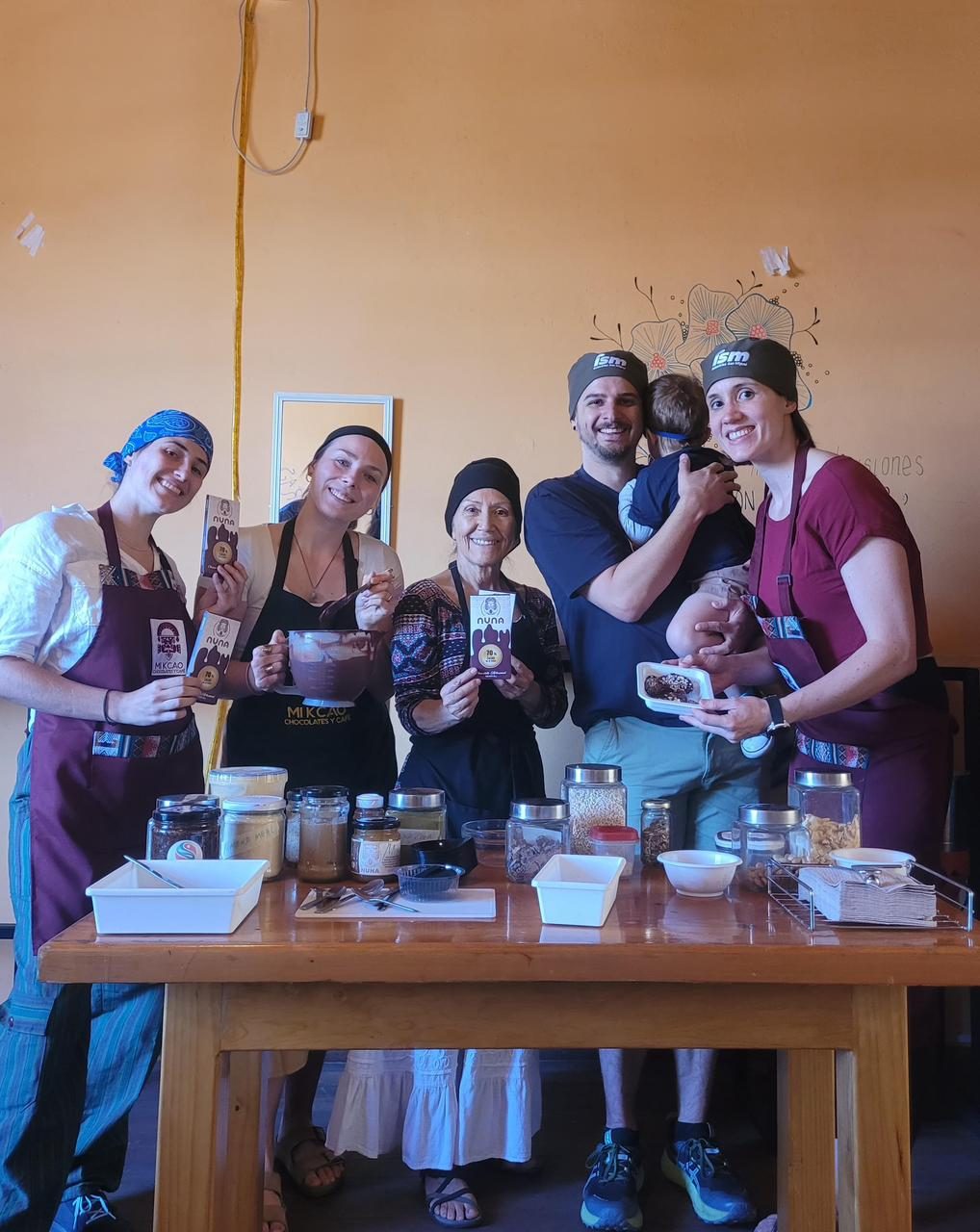Travelers and a baby gathered around a workshop table in Arequipa, holding up the chocolate bars they just made, with jars of Peruvian superfoods and a bowl of melted chocolate in front of them