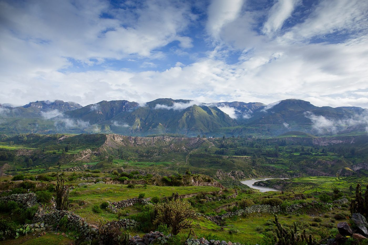 Stone-and-adobe houses of a tiny canyon village surrounded by green pre-Inca terraces