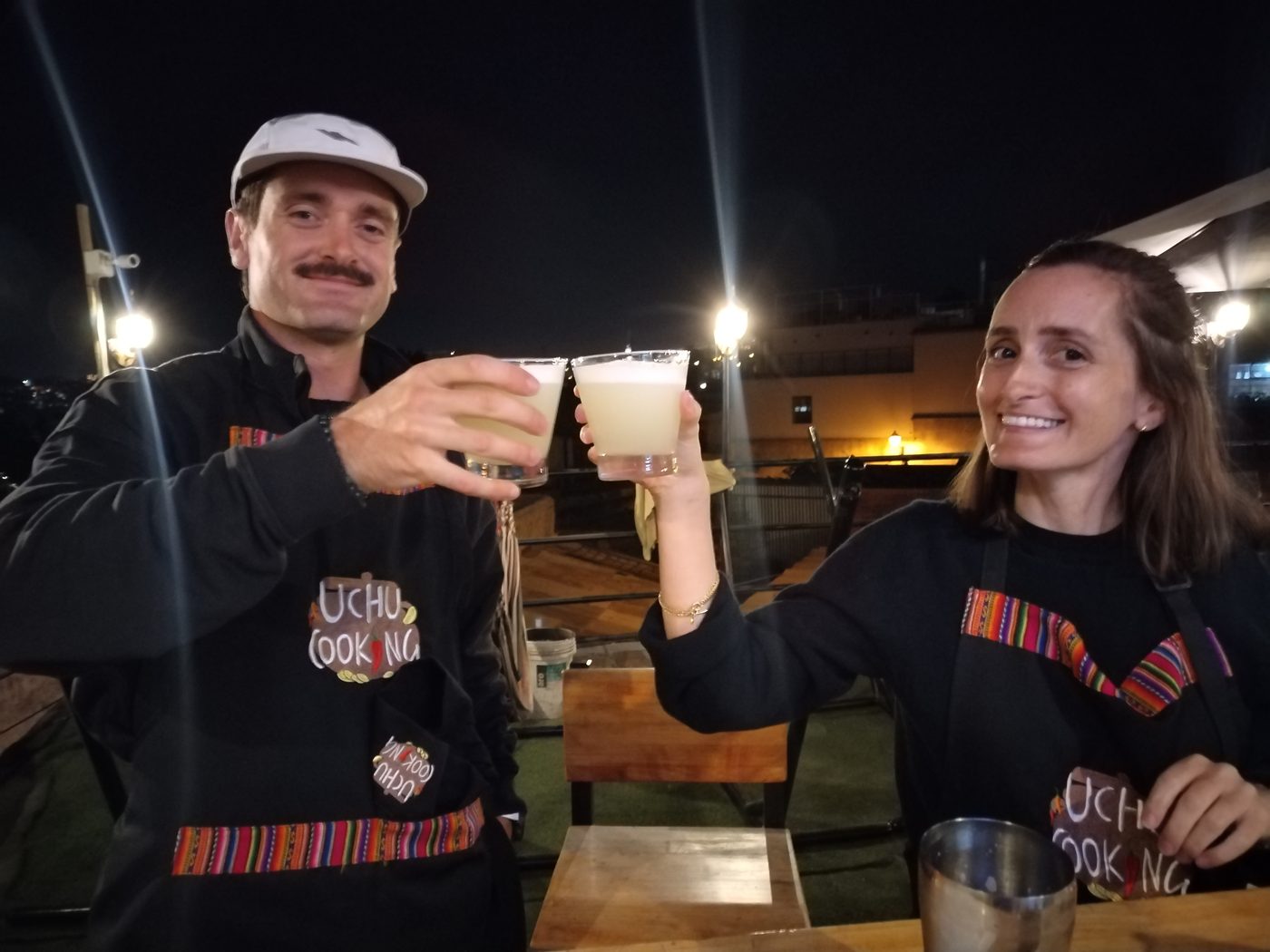 Evening cooking class in Arequipa with smiling guests in aprons raising freshly made pisco sours in a toast