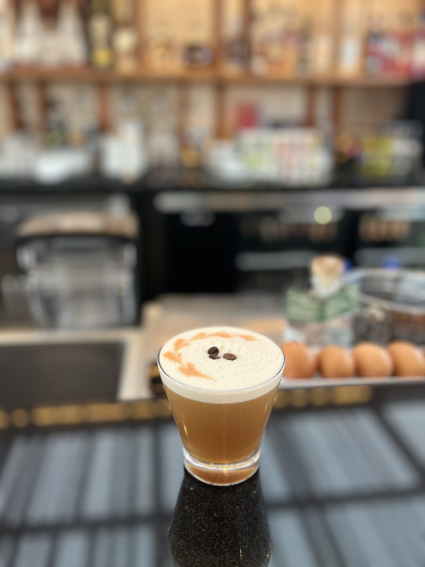 Frothy coffee pisco sour served in a coupe glass on a polished bar counter