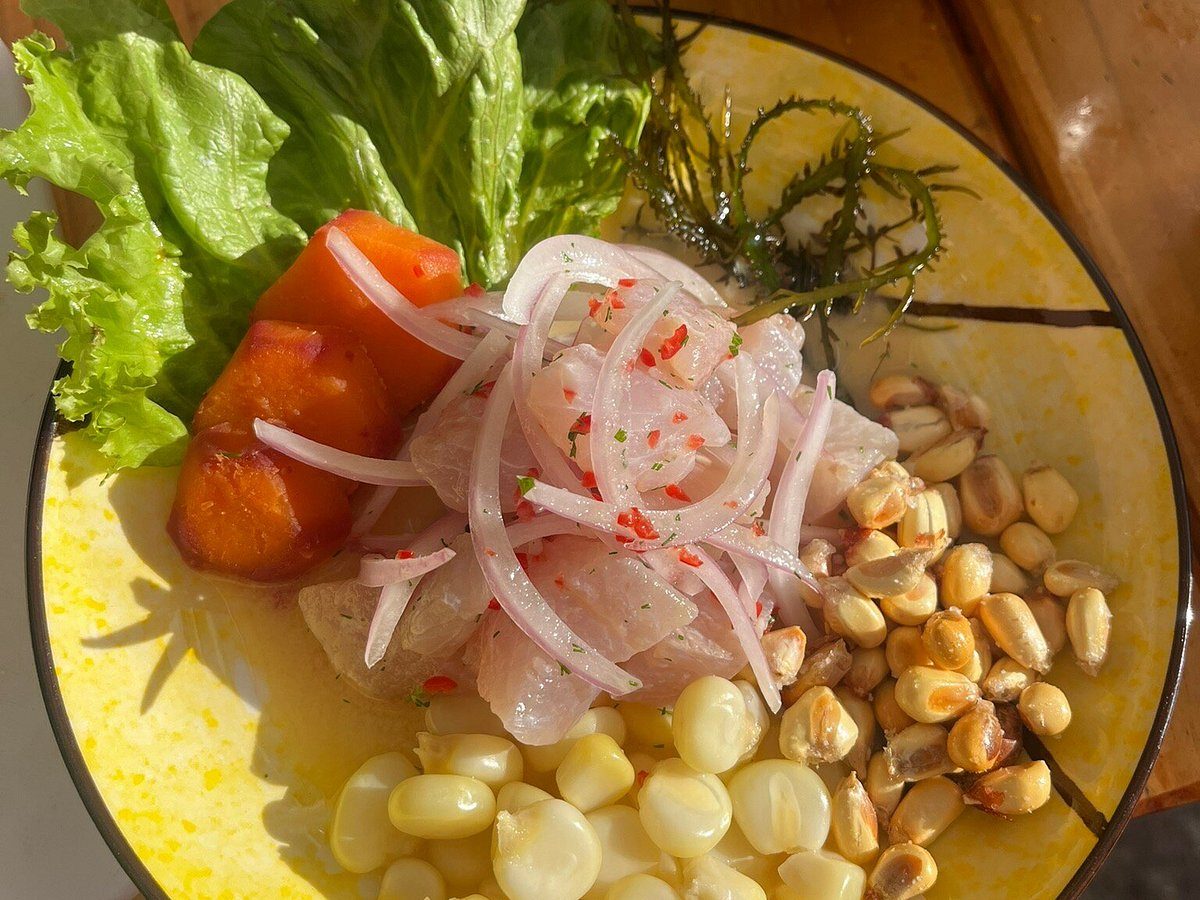 Plated ceviche with red onion, sweet potato, choclo corn and toasted cancha on a yellow ceramic dish