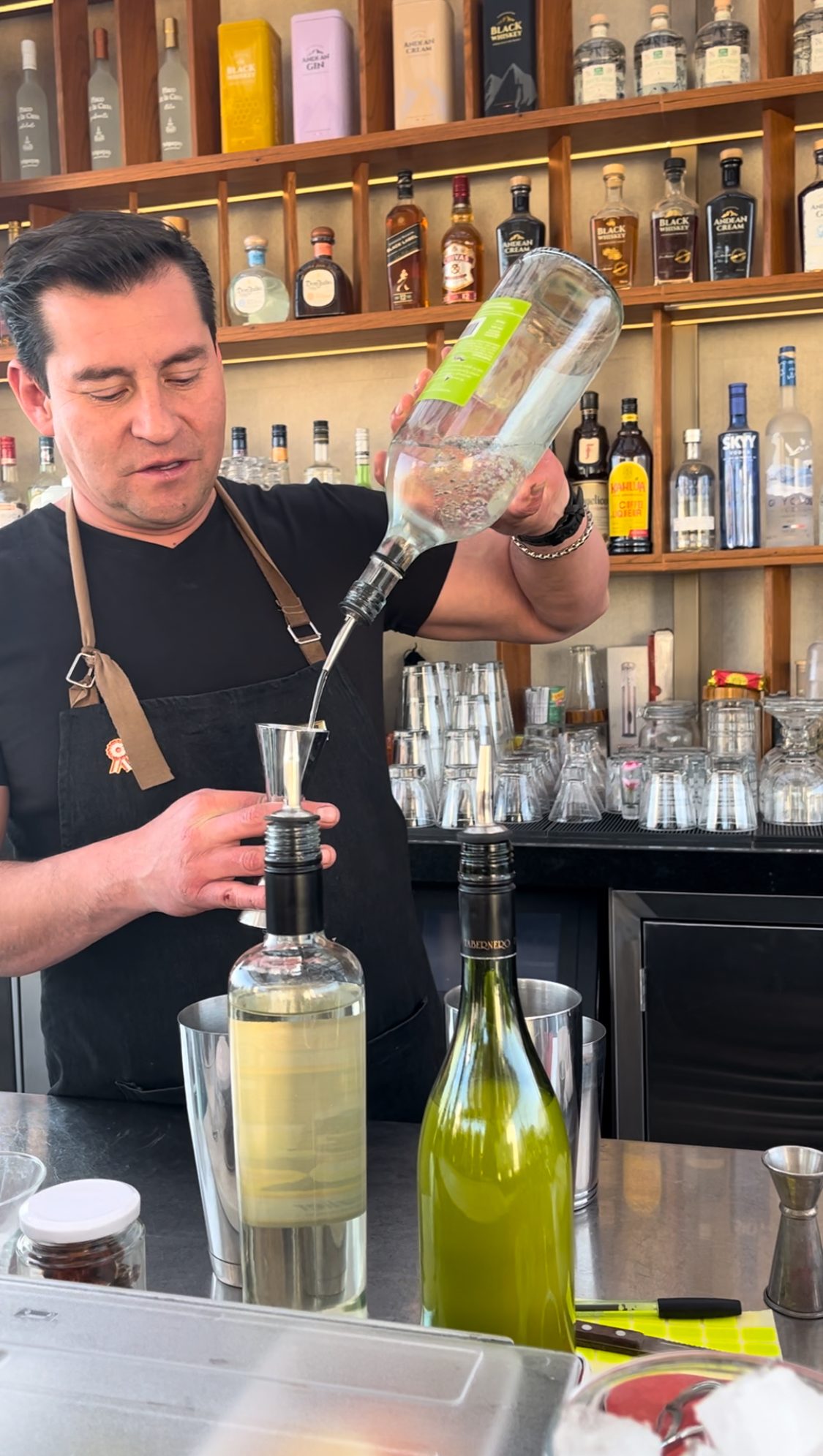 A bartender pouring golden pisco from the bottle into a cocktail shaker during a making class