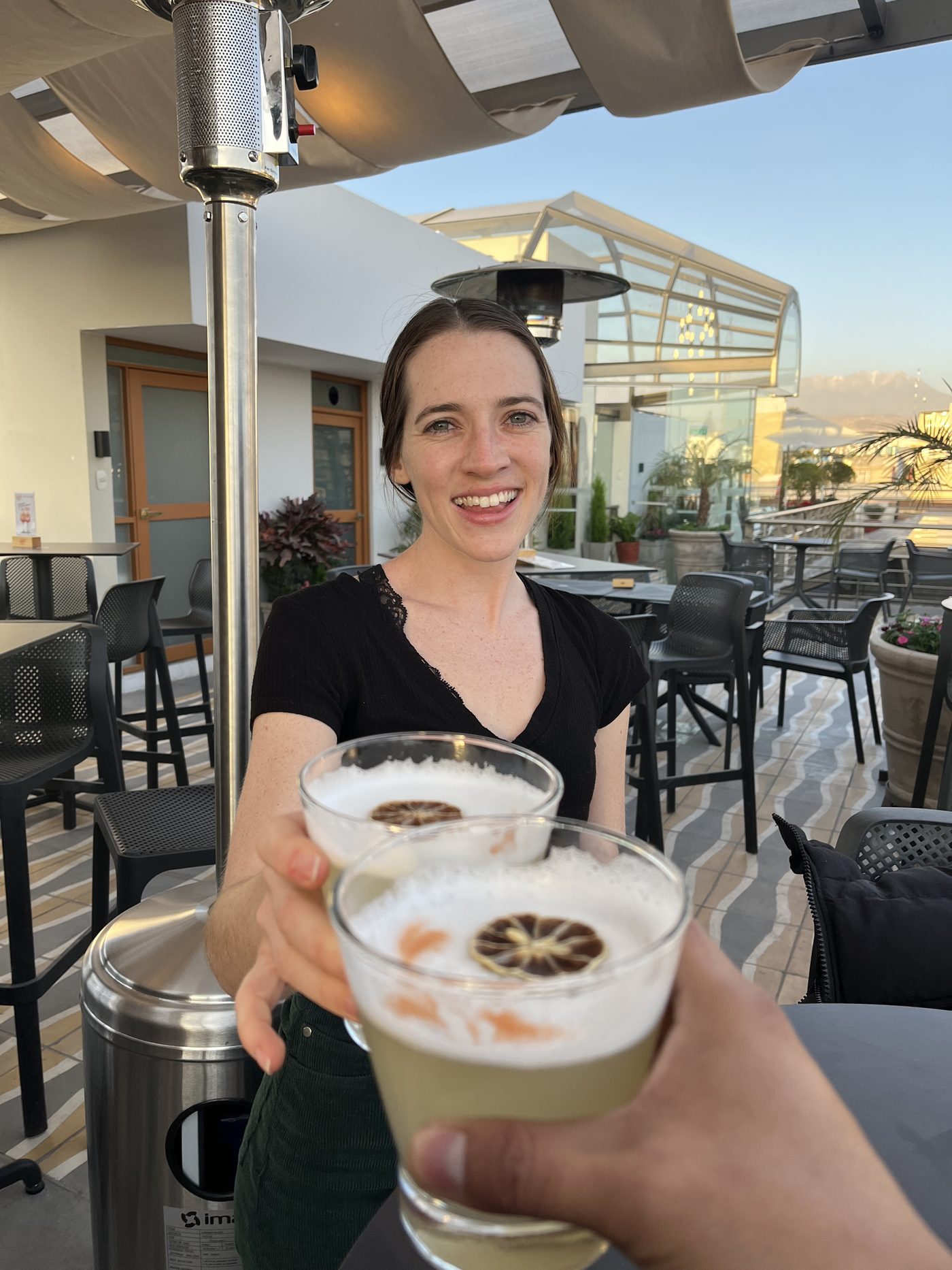 A smiling guest raising a foam-topped pisco sour on a rooftop terrace above Arequipa's white sillar rooftops