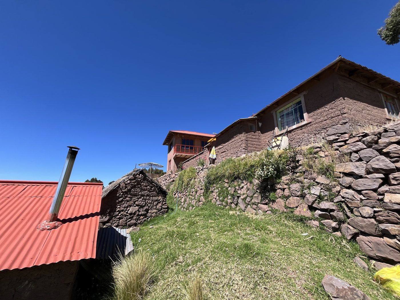Adobe houses with red roofs standing above dry stone walls and grassy terraces on Taquile Island