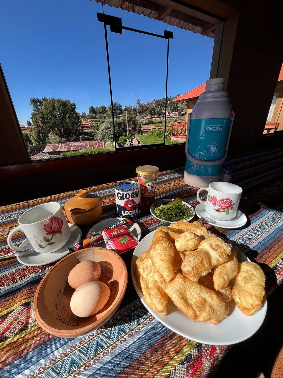 Breakfast of warm bread, boiled eggs and fresh herbs for tea laid on a striped woven tablecloth by a window looking over Taquile's terraces