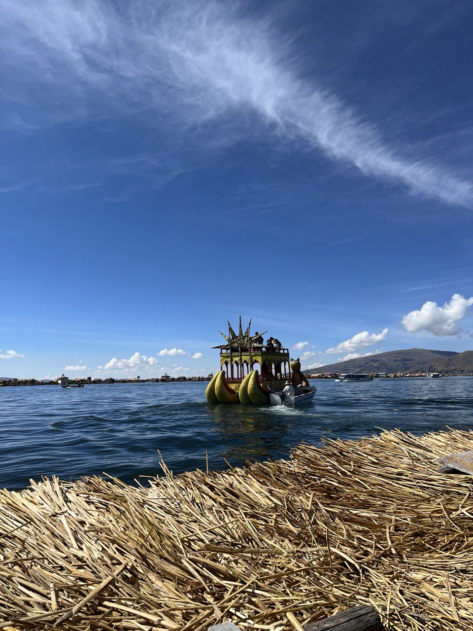 Totora reed boat with a carved prow crossing the deep blue water beside the floating Uros islands